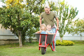 Poster - Father pushing wheelbarrow with his kids outdoors