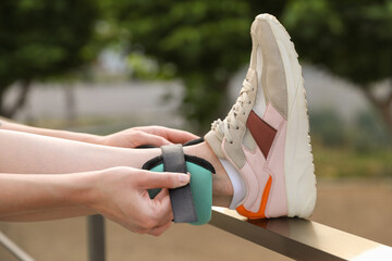 Wall Mural - Woman putting on ankle weight outdoors, closeup