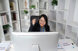 © wichayada - Successful Businesswoman Working on Computer in Modern Office with Bookshelves and Plants, Celebrating Achievement