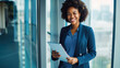 © GraysonStock - A middle-aged afro-american businesswoman standing holding a tablet and smiling looking at the camera.