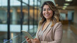 © GraysonStock - A middle-aged Latina businesswoman standing holding a tablet and smiling looking at the camera.