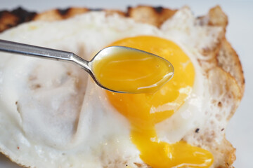 CloseUp of a Spoon with a Runny Egg Yolk on Fried Egg Whites, a tasty and healthy breakfast