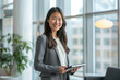 © GraysonStock - A Japanese businesswoman, Asian, happy holding a tablet in a coffee shop, formally dressed.