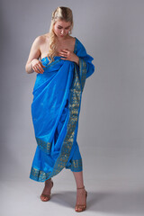 Wall Mural - Pretty blonde woman in blue Indian sari on grey background