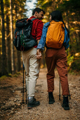 Wall Mural - Happy couple holding hands while hiking together in mountains with backpacks