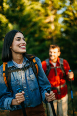 Wall Mural - Couple with backpacks hiking together in forest during sunset