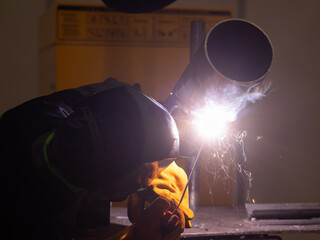 A man wearing a protective mask welds a metal pipe. 