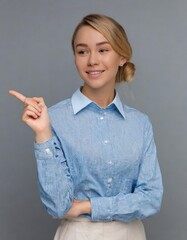 Wall Mural - Happy young smiling professional business woman wearing blue shirt looking at camera pointing finger away at copy space showing aside presenting advertising offer standing isolated at gray background