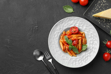 Delicious pasta with tomato sauce, basil and cheese served on black textured table, flat lay. Space for text