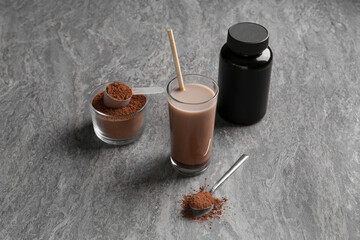 Poster - Delicious protein shake in glass, powder, spoon and plastic bottle on grey table