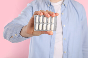 Wall Mural - Woman holding blister with antibiotic pills on pink background, closeup