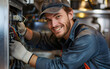 © Marta P. (Milacroft) - Young electrician smiling and fixing a big industrial machine with wires and cables, wearing gloves and workwear