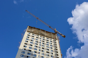 Wall Mural - Tower crane and unfinished building on background of blue sky. Housing construction, apartment blocks in city