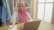 © Krakenimages.com - A muslim woman in a pink hijab gestures during an online conversation in a home office with a laptop and notebooks.