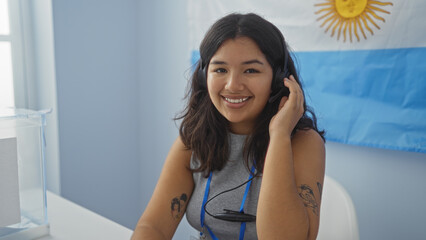 Wall Mural - Young hispanic woman with headphones smiling in an electoral college room with an argentine flag in the background.