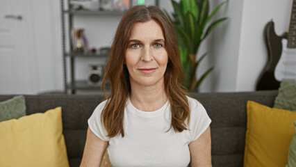 Wall Mural - Middle-aged woman with short hair sitting in a well-lit living room, exuding a calm and mature demeanor.