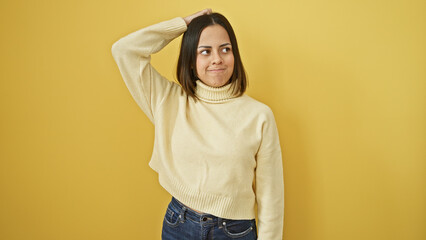 A young hispanic woman with a casual hairstyle poses confidently against an isolated yellow background, exuding beauty and charm.