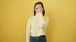 © Krakenimages.com - A young hispanic woman with a stylish hairstyle stands against a yellow wall, covering one eye with her hand.