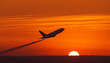 © SolaruS - A commercial airplane flying through an orange sky during sunset, leaving a trail of white exhaust behind and Copy Space