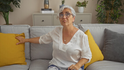 Poster - Grey-haired woman sitting indoors in a living room with yellow cushions on a sofa, showcasing a peaceful home environment with plants and decor.