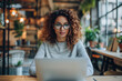 © Bank-adtapon - A young woman with curly hair and glasses is deeply focused on her laptop in a stylish modern office The soft lighting and greenery create a productive and inviting workspace, generative ai