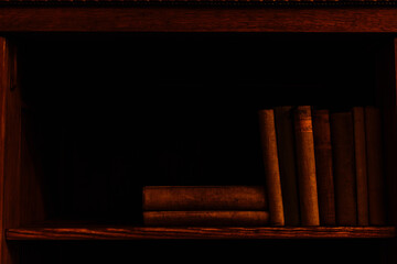 Ancient books lying on a dark shady shelf in an old classic mansion. Antique library and old literature concepts.
