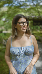 Wall Mural - Beautiful hispanic woman with glasses, carefree and smiling, looking around a traditional japanese park, radiating positivity and joy.