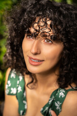 Beautiful woman with dark curly hair among fresh green leaves