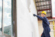 © tong2530 - A painter applies a layer of white paint to a wall using a roller.