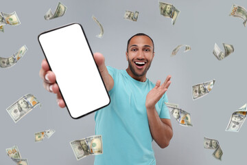 Wall Mural - Happy man showing mobile phone with empty screen under money rain on grey background