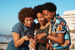 © Chanelle2000/peopleimages.com - Meme, phone or social media with friends on beach together for summer holiday, travel or vacation. App, relax and text message with group of happy women outdoor on coast for bonding or weekend fun