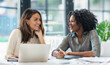 © Igor - Happy professional women collaborating with enthusiasm in a modern bright office setting. Two diverse female entrepreneurs using a laptop for a productive business meeting in a corporate workplace.