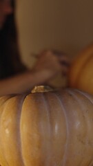 Wall Mural - Vertical video. Preparing for Halloween, by Candlelight, the Woman Making a Jack-o'-Lantern from a Pumpkin, Background Out of Focus. Pumpkins on the Table.