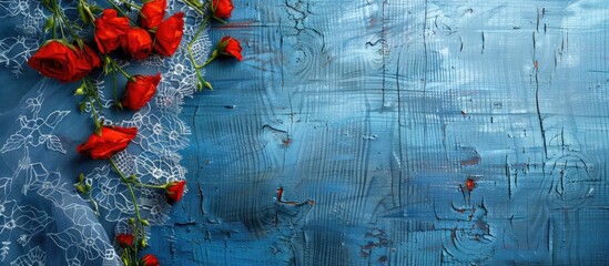 Wall Mural - Top view of red flowers on a lace tablecloth over a blue wooden table with copy space image