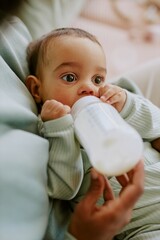 High angle shot of baby boy eating formula while his mother holding bottle and helping him to eat