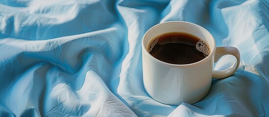 Wall Mural - Morning scene with a white cup of black coffee set against a blue textile background ideal for a copy space image