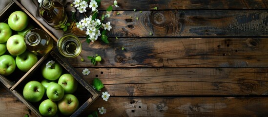 Leinwandbilder - Top view of a wooden table with a wooden box filled with ripe green apples a branch of white flowers and a glass and bottle of cider with copy space image