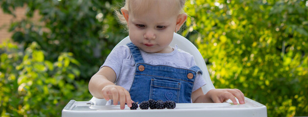 Wall Mural - little happy girl eating blackberry. Selective focus