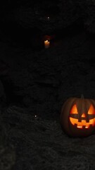 Wall Mural - Vertical video. Halloween Pumpkin at the Cave Entrance on Sharp Rocks, Decorated with Burning Candles. All Saints' Day Background.