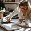 © Miso Ai - A woman in glasses writes in a notebook at a desk surrounded by books and a cup of coffee.