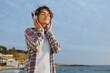 © ViDi Studio - Side view young dreamful calm woman she wear shirt casual clothes listen to music in headphones close eyes rest on sea ocean sand shore beach outdoor seaside in summer day free time Lifestyle concept