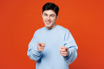 Wall Mural - Young smiling happy man he wears blue sweatshirt casual clothes point index finger camera on you motivating encourage isolated on plain red orange color background studio portrait. Lifestyle concept.