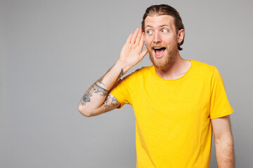 Young curious nosy Caucasian man he wearing yellow t-shirt casual clothes try to hear you overhear listening intently look aside isolated on plain grey background studio portrait. Lifestyle concept.