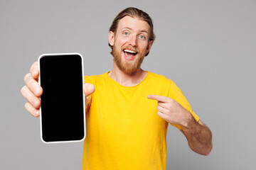 Young man he wear yellow t-shirt casual clothes hold in hand use point index finger on mobile cell phone with blank screen workspace area isolated on plain grey background studio. Lifestyle concept.