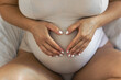 © puhimec - Pregnant woman making heart with hands on her belly on bed.