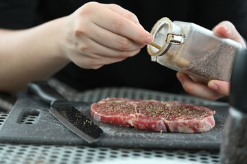 Close-up of hands carefully adding salt seasoning to a raw steak, preparing it for cooking