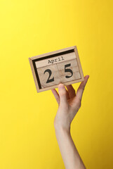 Wooden block calendar with date april 25 in hand on yellow background