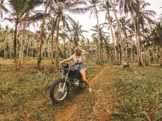 Young woman riding a motorcycle through a tropical palm tree forest.