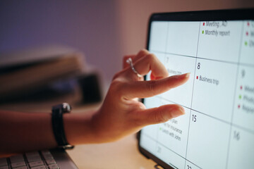 Closeup of a hand interacting with a digital calendar on a tablet screen, planning and organizing meetings and business trips reflected on screen planner