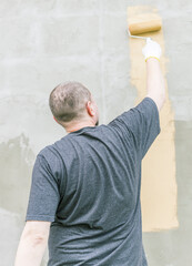 Wall Mural - A man in a grey t-shirt paints a vertical stripe on a concrete wall.